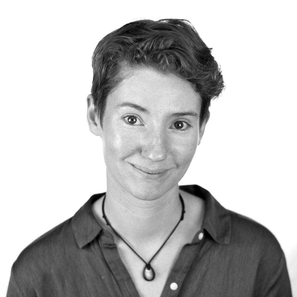 A black and white photograph of Lucy Bellwood. She has short curly hair and wears a button-down shirt.