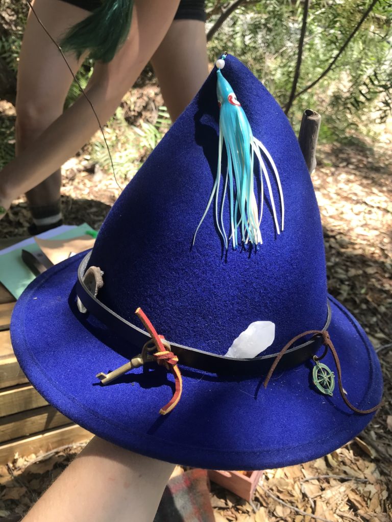 A pointy blue felt hat with a variety of nautical items attached to it.