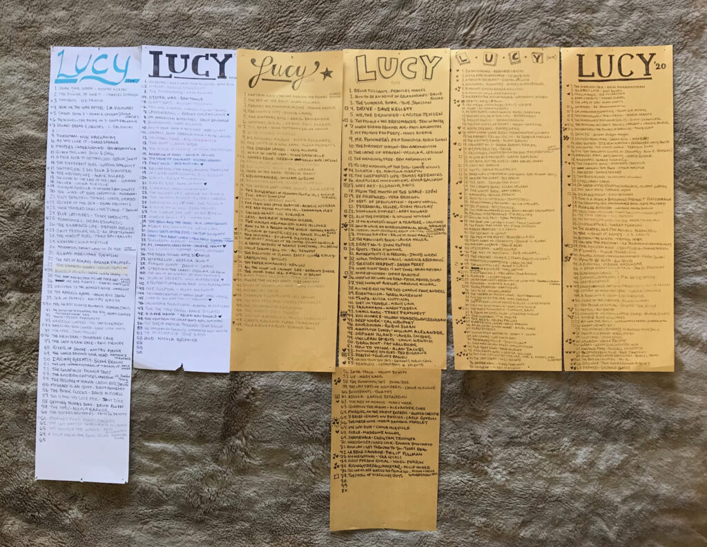 A collection of six tall, thin pieces of paper with lists of books written on them. They're dated from 2015 to 2020 and have the name Lucy at the top of each one.