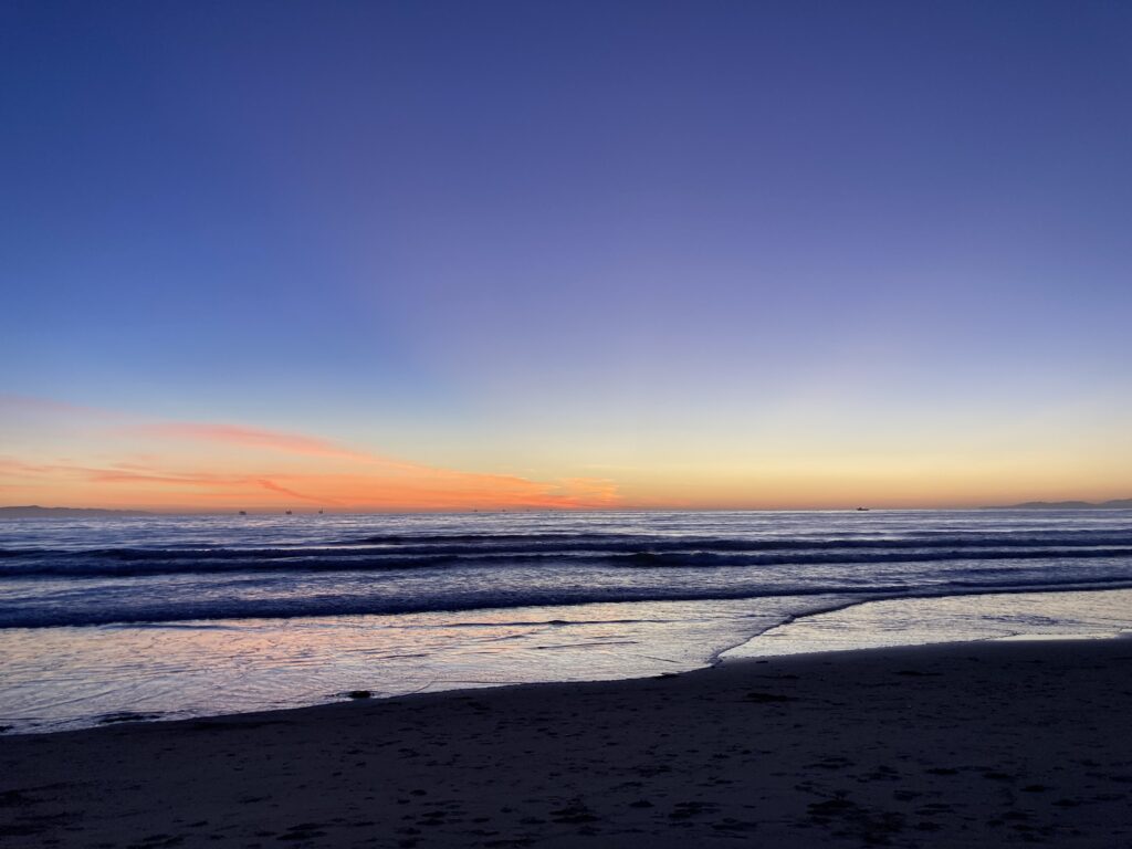 A gleaming ocean at sunset. The sky is blue fading into fiery apricot at the horizon.