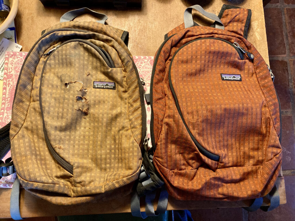 Two small Patagonia backpacks side by side. They're identical, but the one on the left is faded to a light brown with tears across the front. The one on the right is newer-looking, vibrant orange.