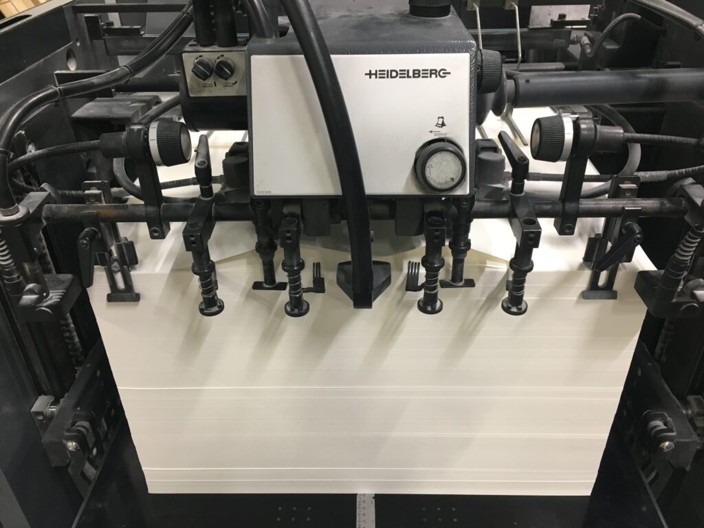 A complex offset press housing a huge stack of blank paper.