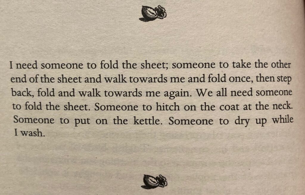 A page from a book that reads: I need someone to fold the sheet; someone to take the other
end of the sheet and walk towards me and fold once, then step
back, fold and walk towards me again. We all need someone
to fold the sheet. Someone to hitch on the coat at the neck.
Someone to put on the kettle. Someone to dry up while
I wash.