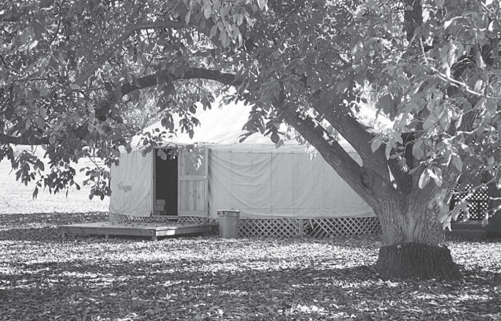A greyscale photo of a yurt nestled under trees.
