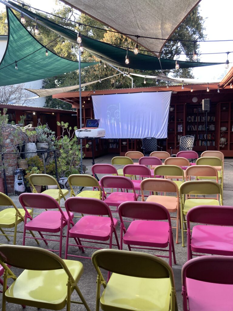 A bright collection of pink and green folding chairs set up in the courtyard of an open air bookstore.