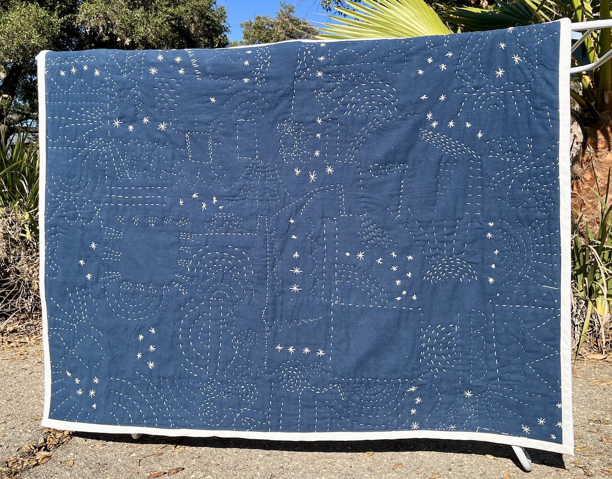 A blue quilt back with intricate white embroidery looking like stars.